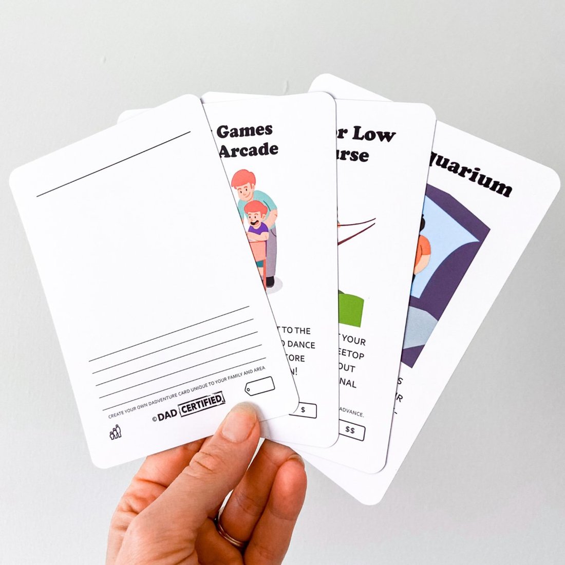 A hand holding the Dadventure cards fanned out, including a blank create-your-own card in front