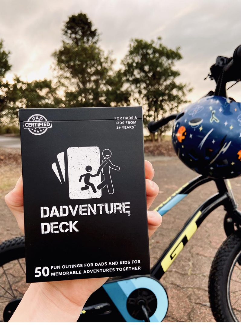 The Dadventure Deck box held up outdoors beside a child's bike, ready for the next adventure